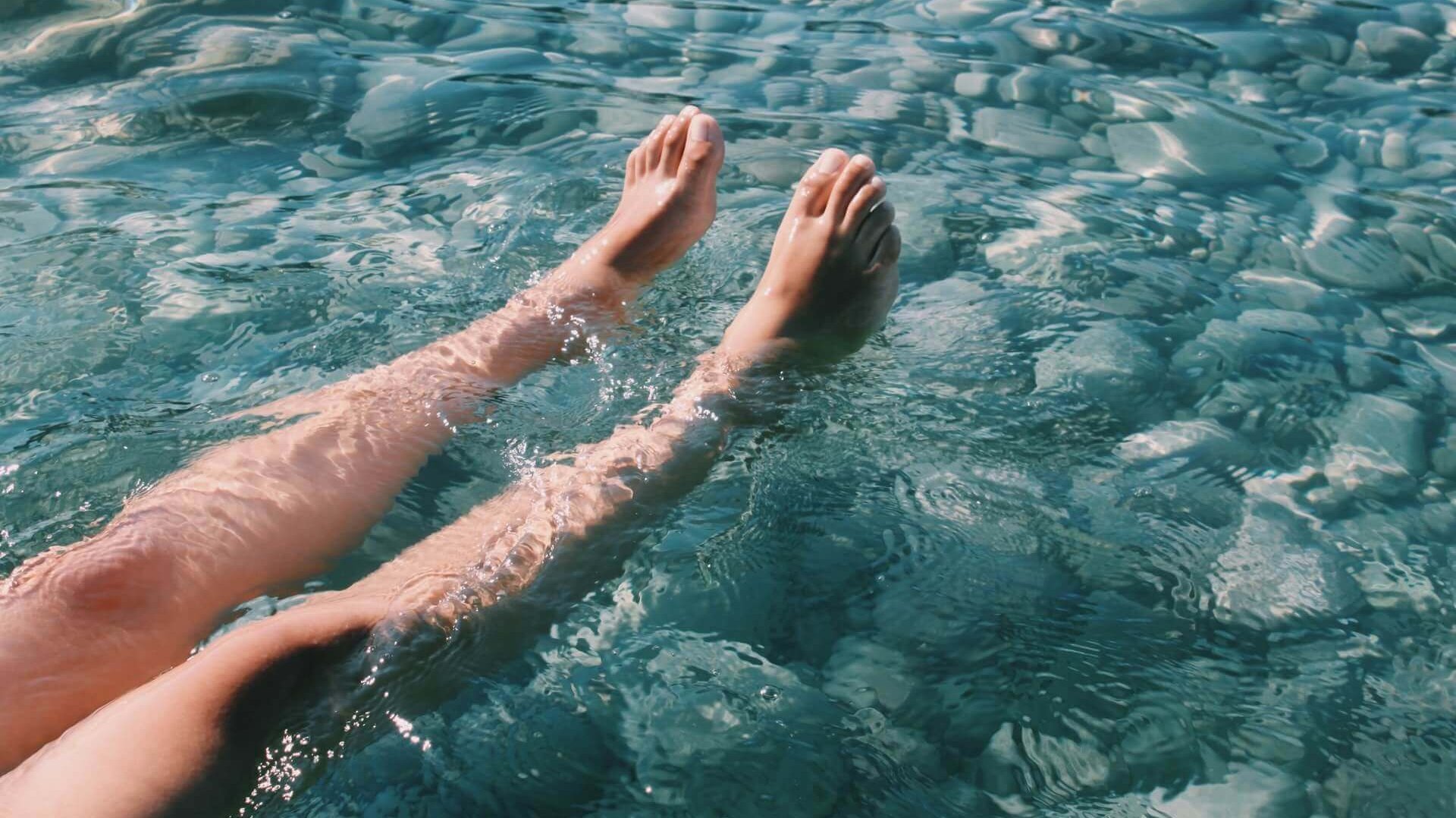 Das Bild zeigt zwei Beine, die sich im kalten Wasser abkühlen. 