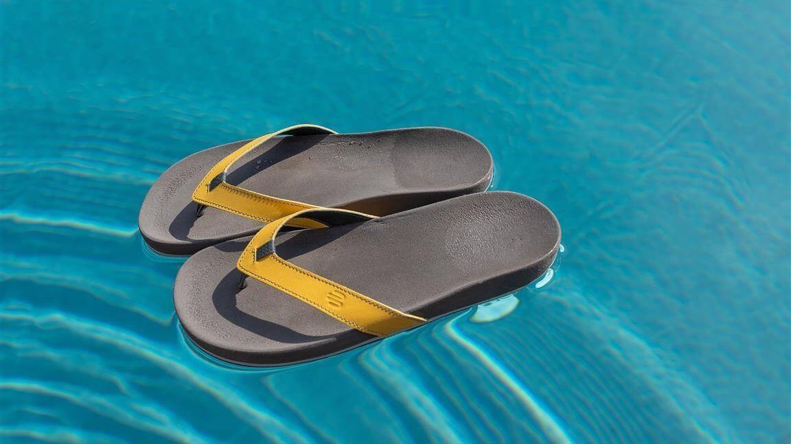 Das Bild zeigt ein Paar ErgoPad:ID Zehentrenner auf der Wasseroberfläche eines Pools. Die ergonomische Sandale bietet individuelle Unterstützung für die Füße.